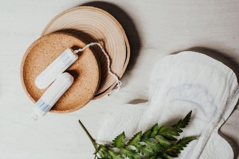 Tampons and a sanitary pad arranged on a neutral background, symbolizing menstrual health and the importance of supporting your cycle with real food.